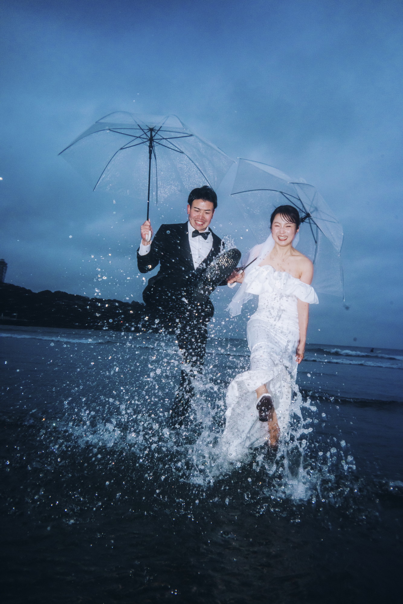 雨の七里ヶ浜で波を蹴り上げて遊ぶウェディングフォト