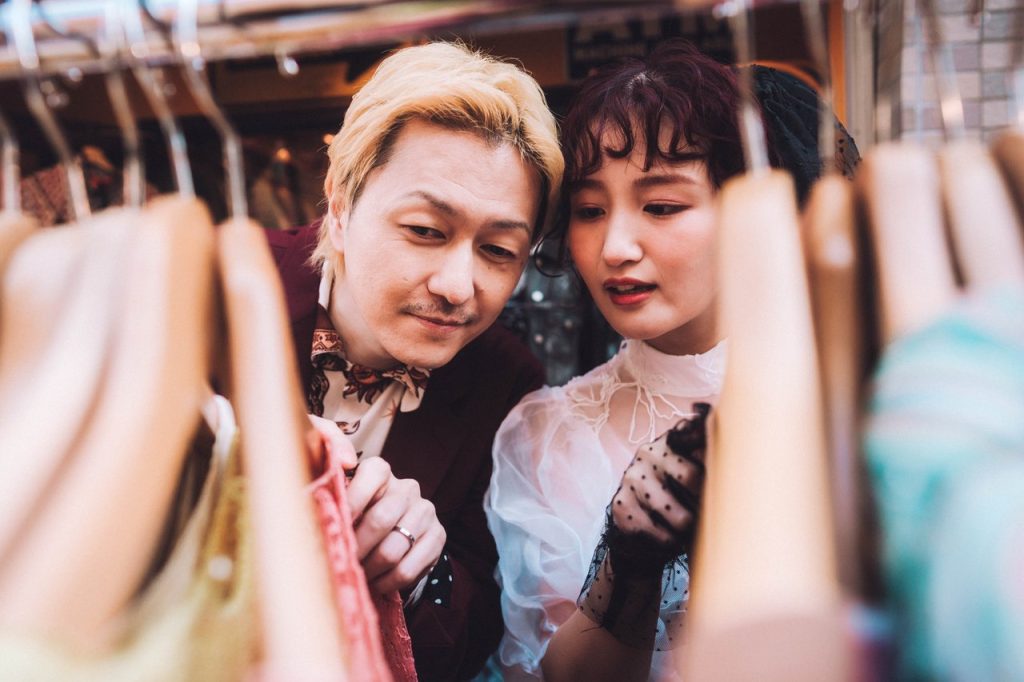 Pasangan saling menatap di sela-sela gantungan baju di toko vintage